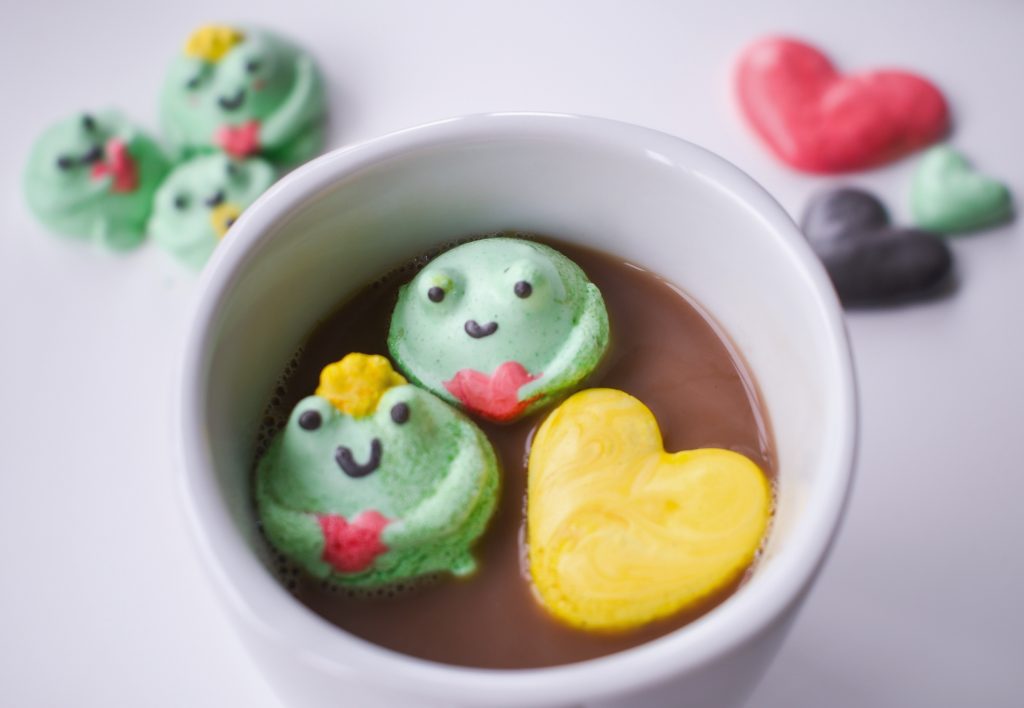 Photo of frog meringue cookies floating on top of hot chocolate. 