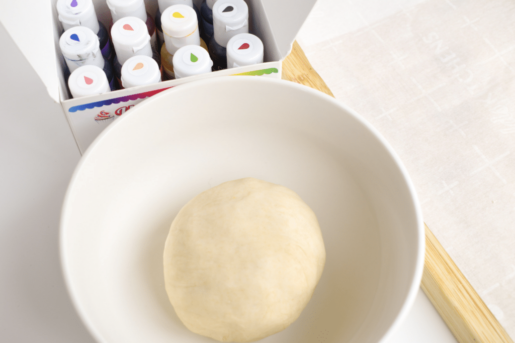 Photo of ball of dough in a bowl and various gel food coloring bottles 