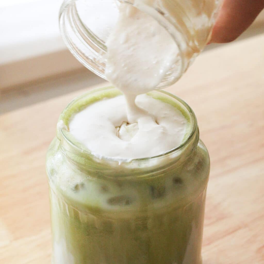 Pouring banana cold foam over matcha latte.