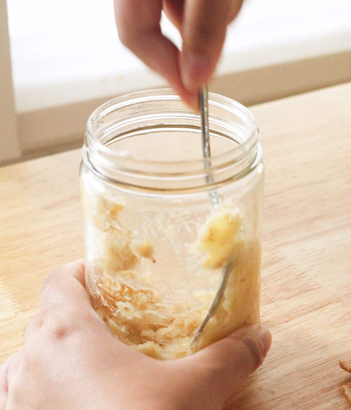 Mashing a banana on the side of a glass jar with a fork.
