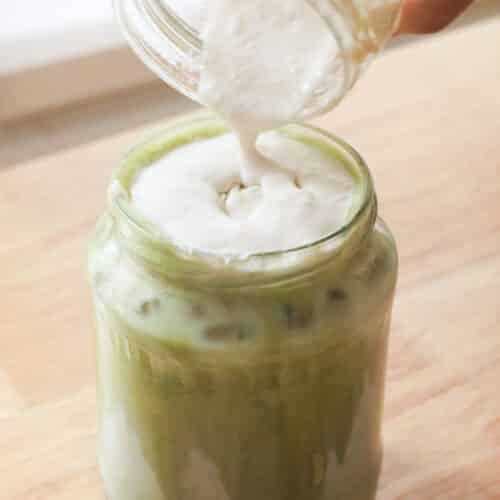 Pouring banana cold foam over matcha latte.