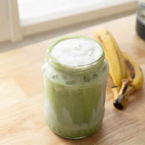 Matcha latte topped with banana cold foam in a glass jar.