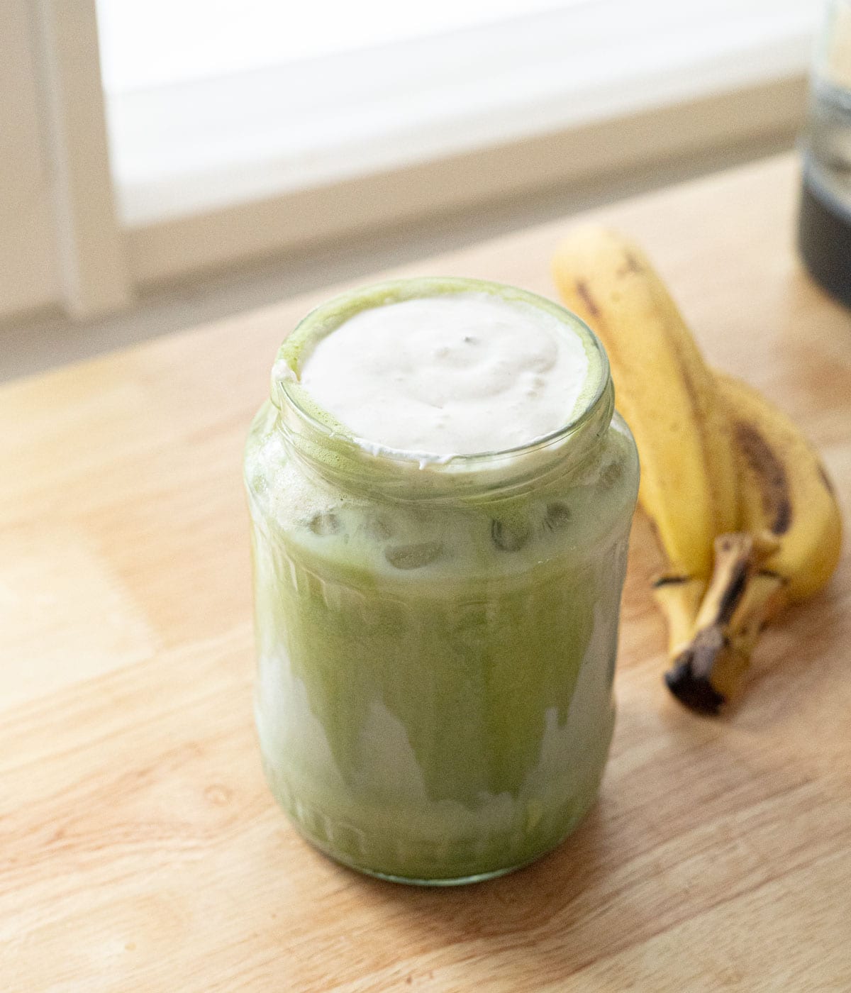 Matcha latte topped with banana cold foam in a glass jar.