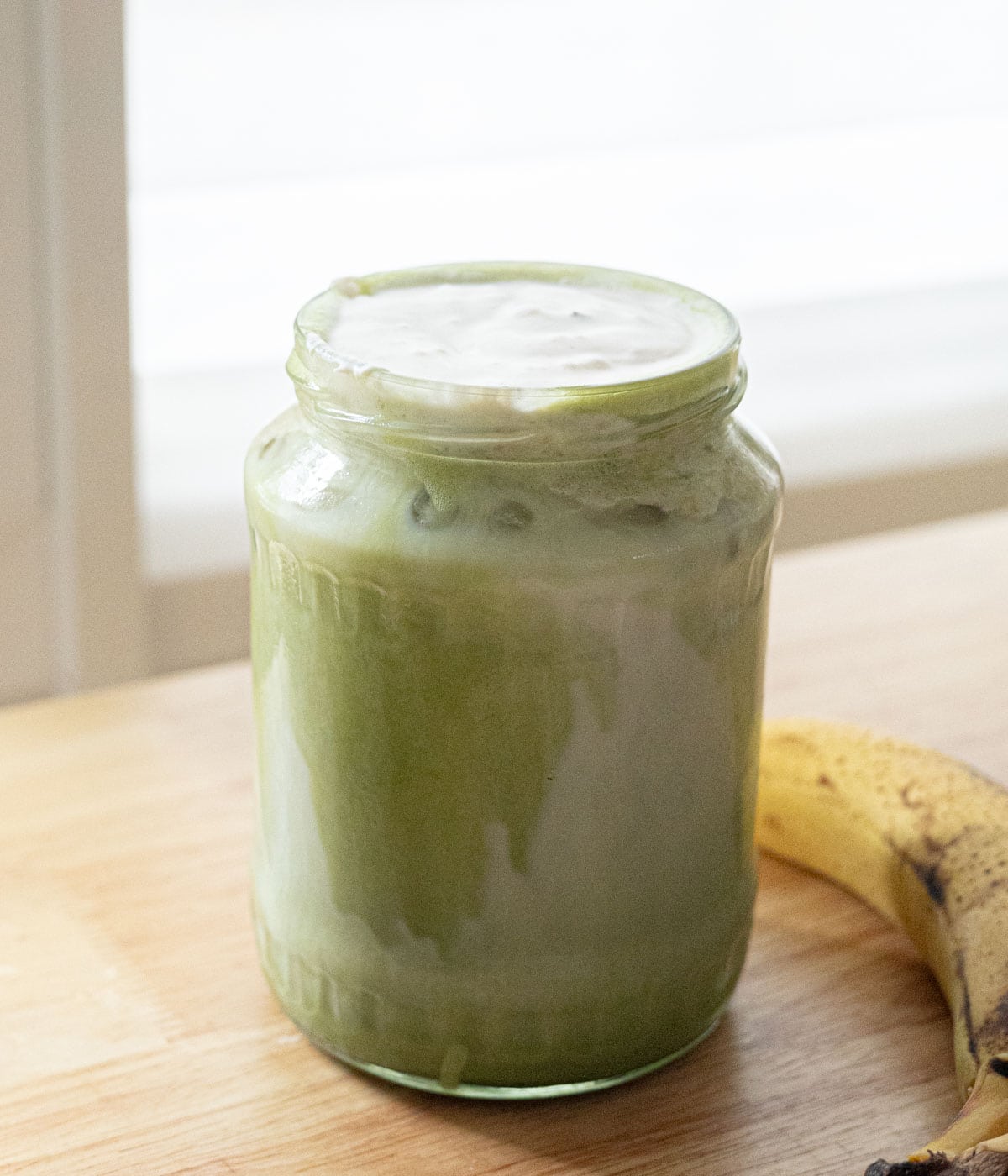 Matcha latte topped with banana cold foam in a glass jar.
