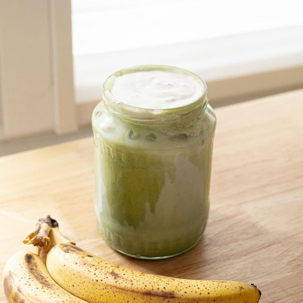 Matcha latte topped with banana cold foam in a glass jar.
