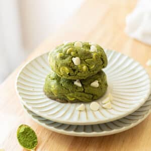 Chunky white chocolate matcha cookies on a fluted white plated on top of a wooden island.