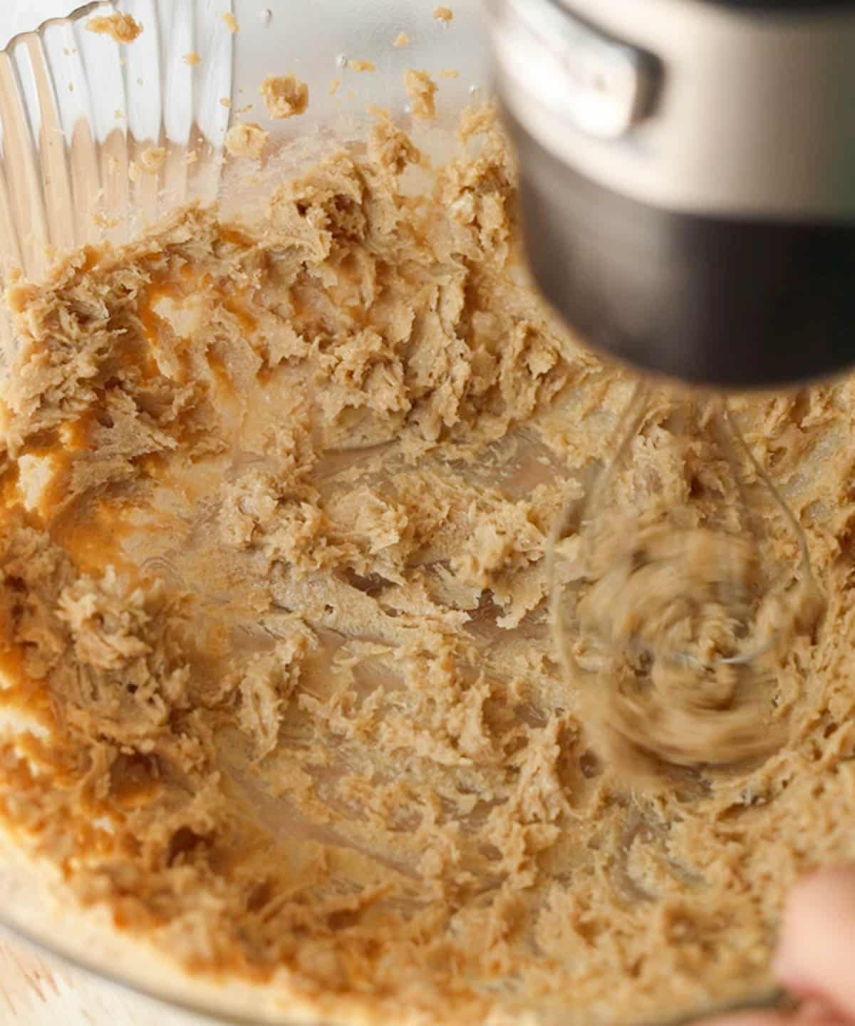 Mixing butter and sugar in a glass bowl with a hand mixer.