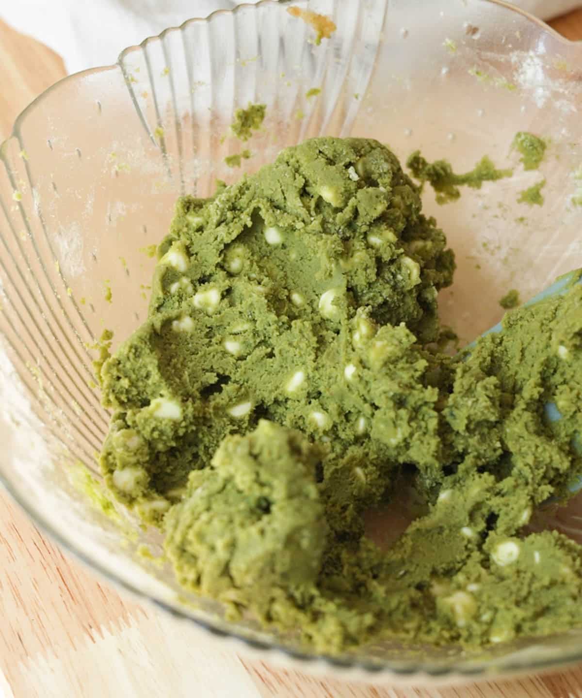 Green matcha cookie dough white chocolate chips in a glass mixing bowl, ready to be scooped.