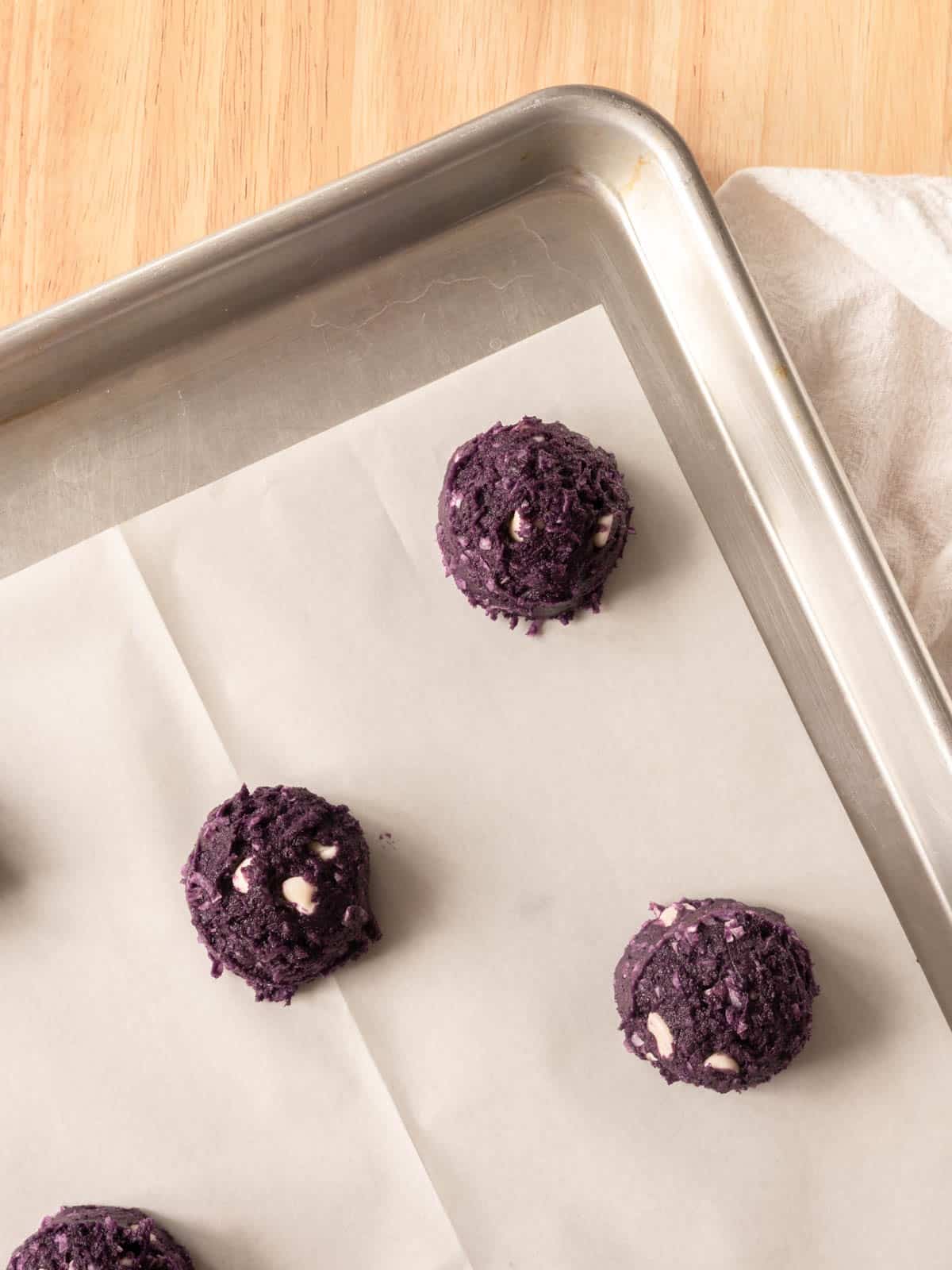 Ube cookies scooped onto a lined baking tray.