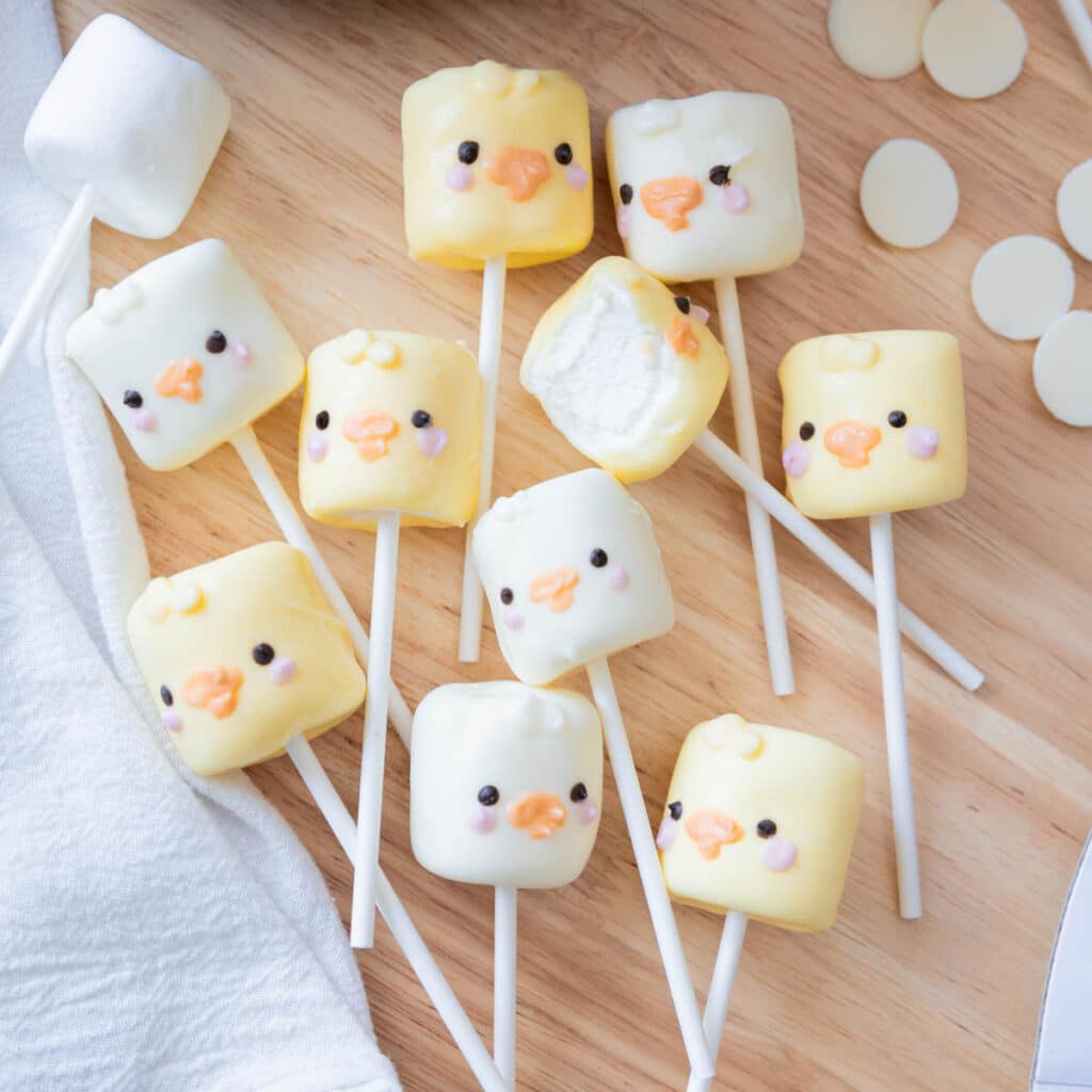 Adorable spring marshmallow pops on a stick decorated as ducks and chicks, all on a wooden backdrop.