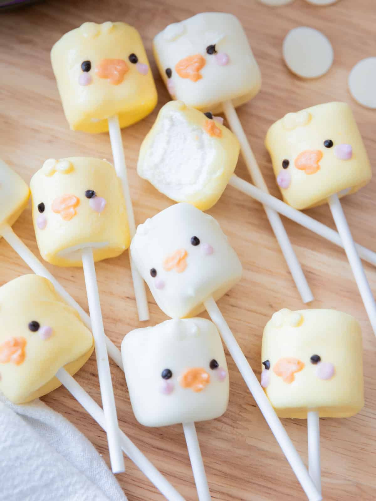 Adorable spring marshmallow pops on a stick decorated as ducks and chicks, all on a wooden backdrop.