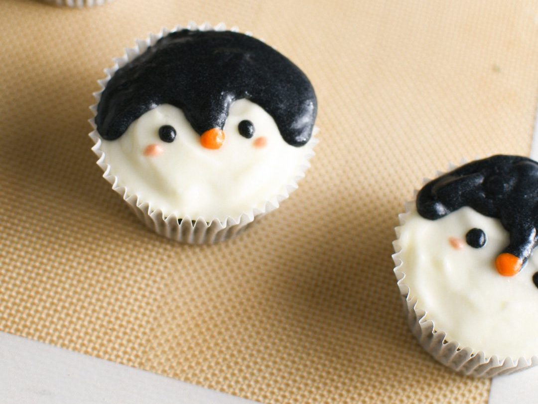 Two penguin cupcakes on top of a silicone mat 