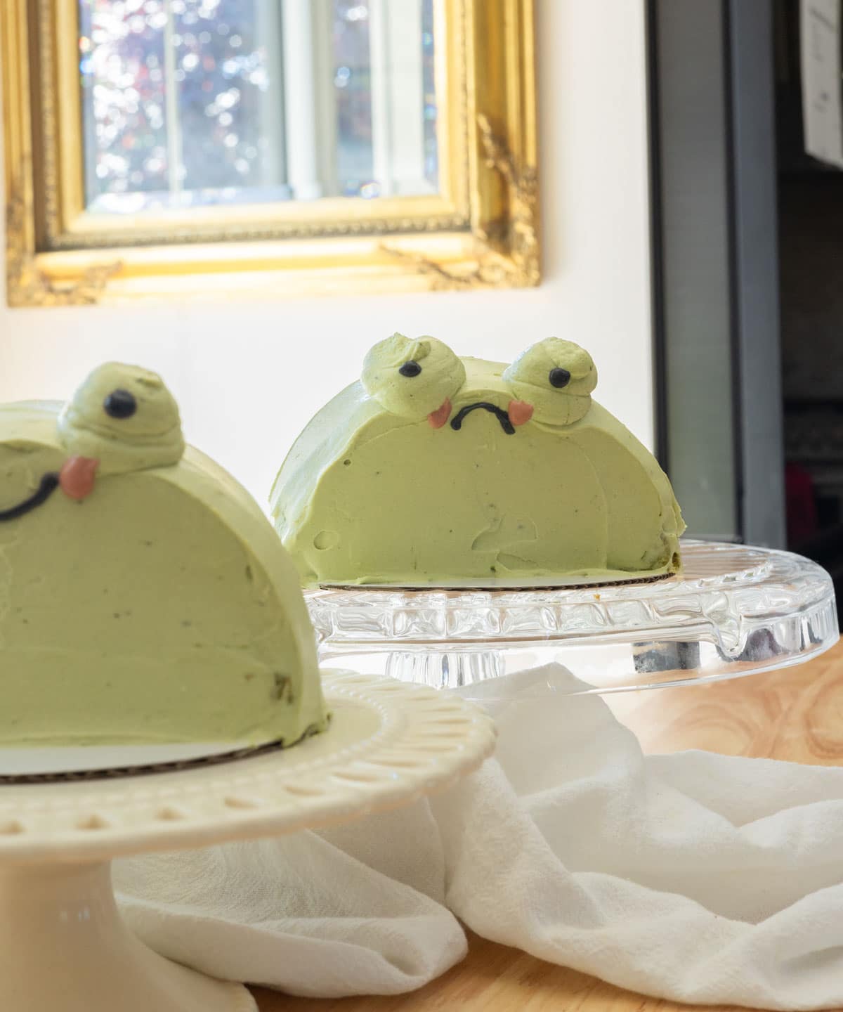 Two frog cakes on cake stands.