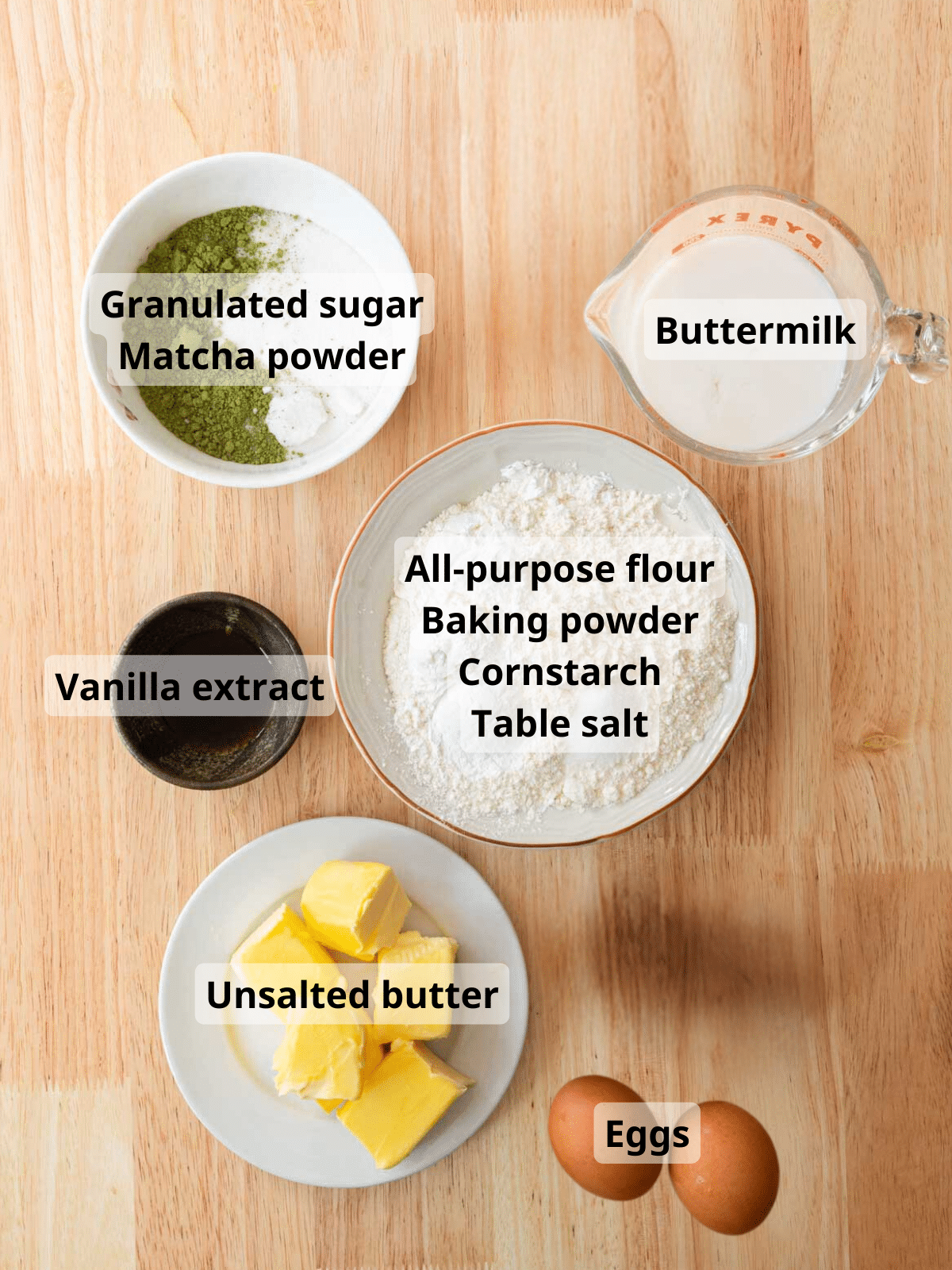 Matcha cake ingredients on a wooden backdrop with labels.