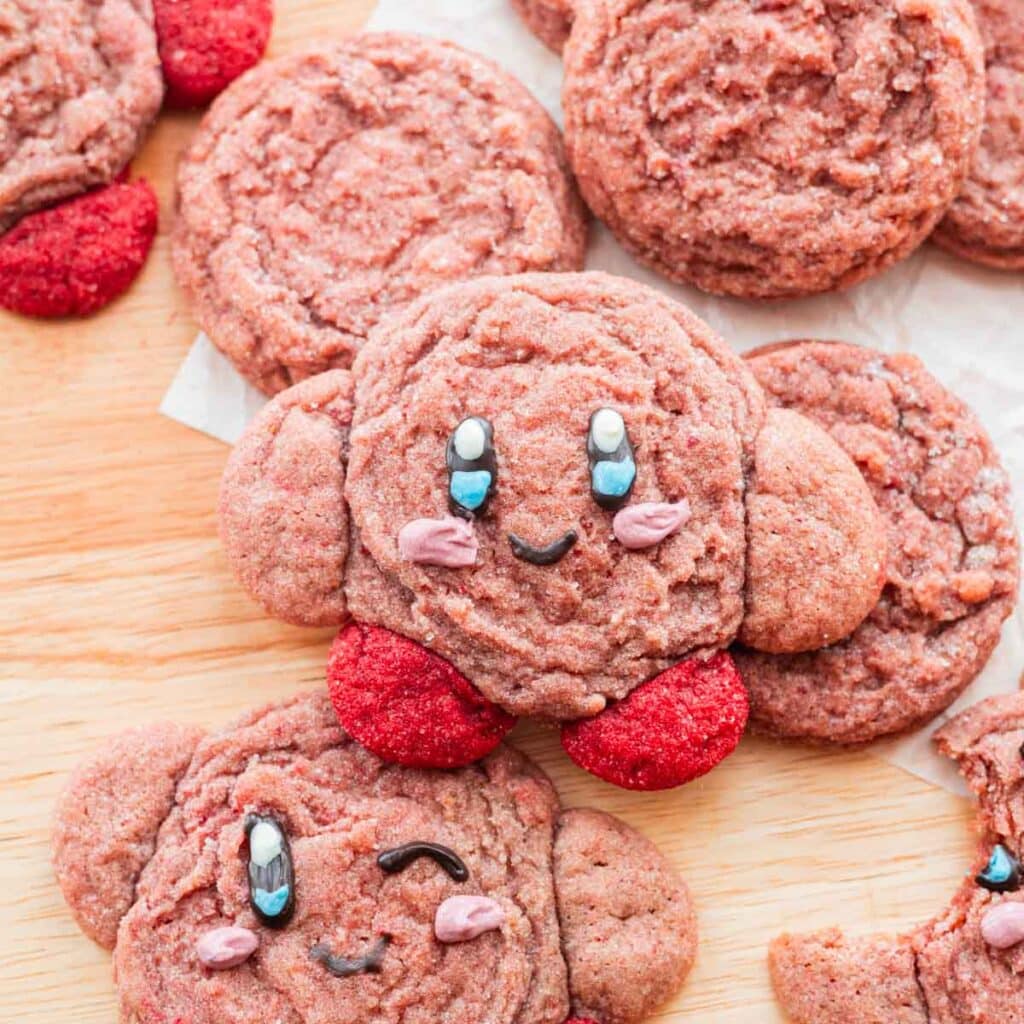 Strawberry kirby cookies spread out on a wooden island.