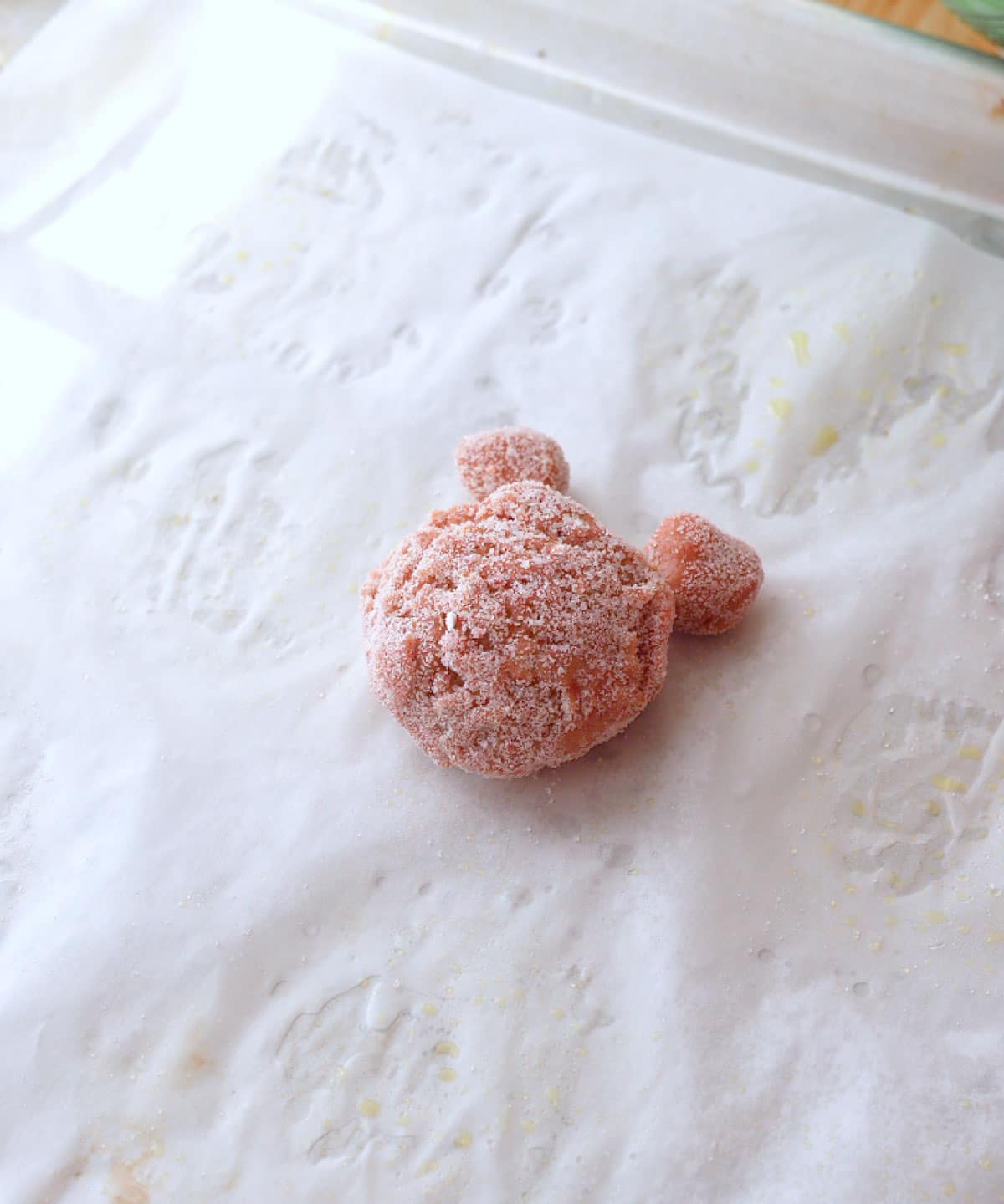 Strawberry cookie dough ball with ears rolled in sugar ready to be baked.