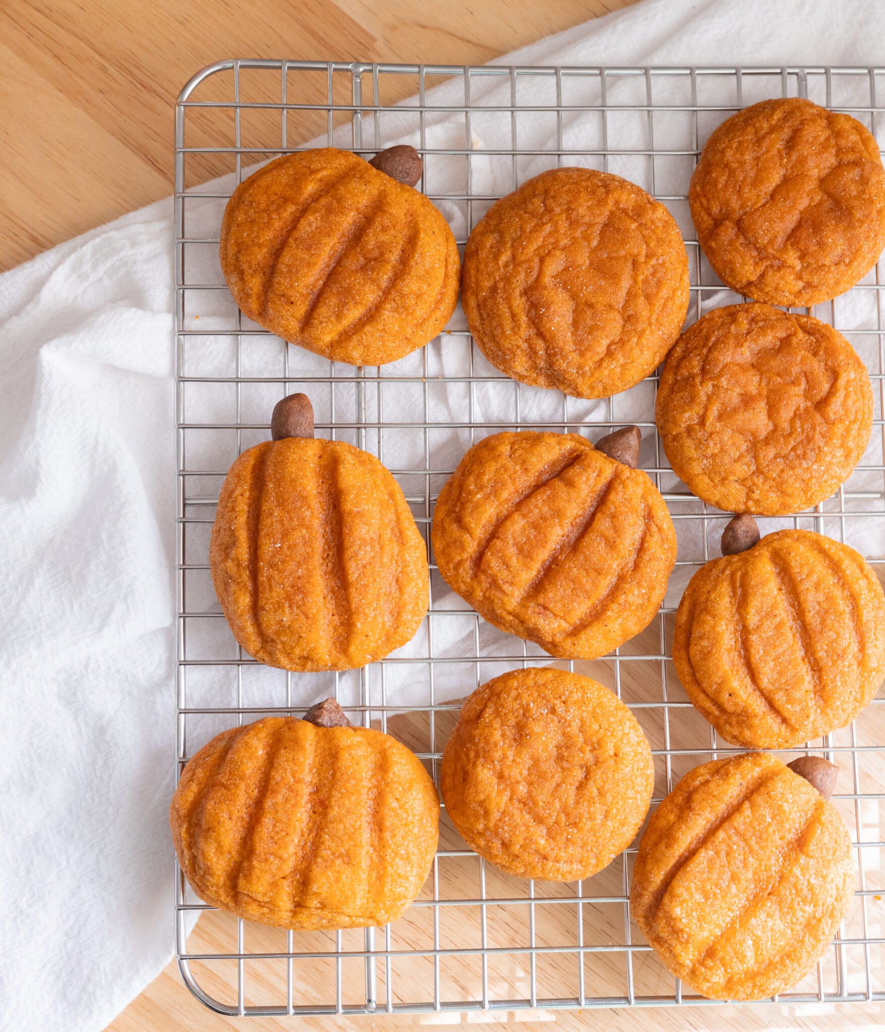 Cute pumpkin-shaped pumpkin snickerdoodle cookies on a wire rack.