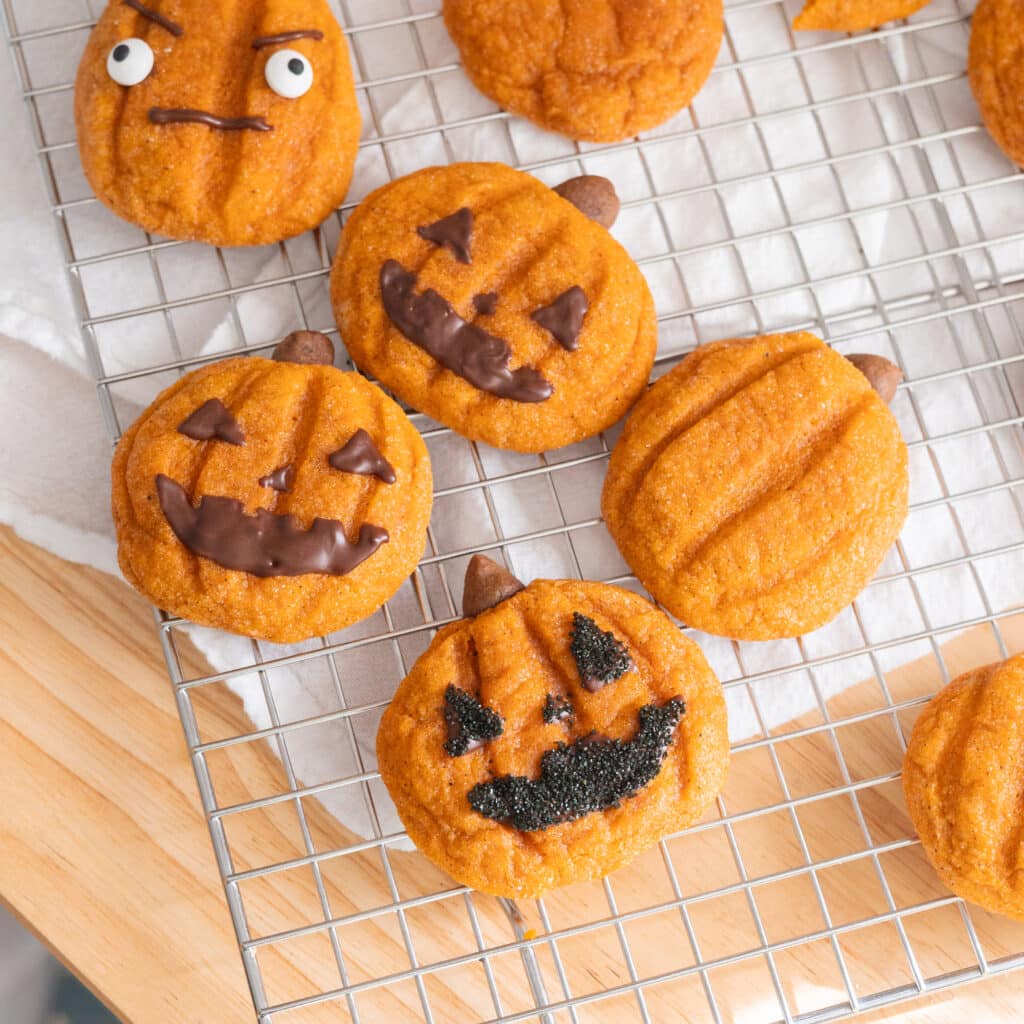 Cute jack o'lantern pumpkin snickerdoodles on a wire rack.