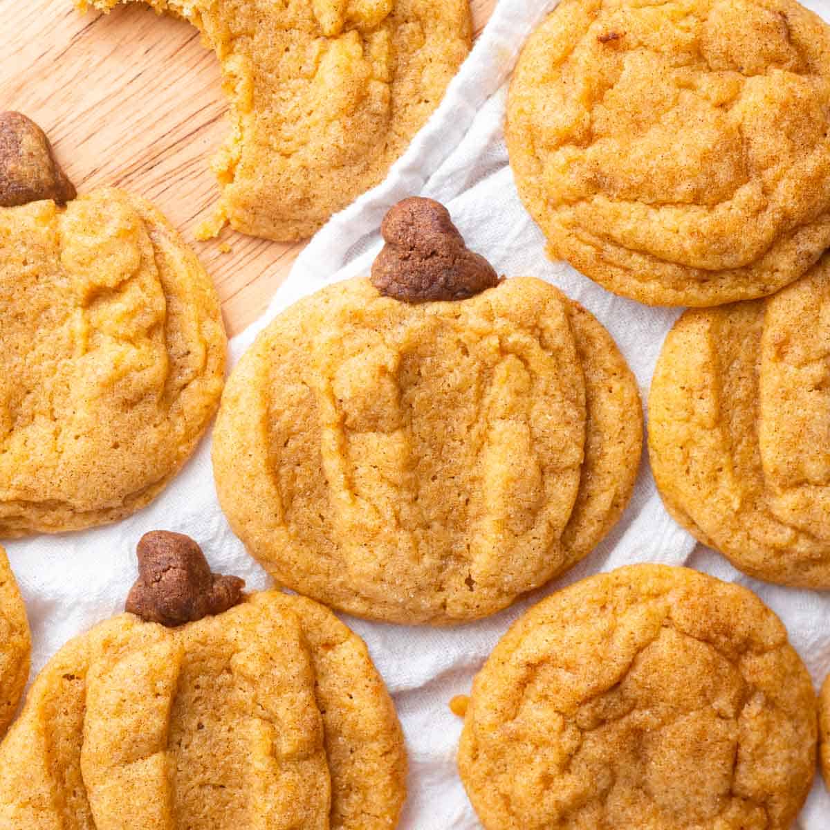 Pumpkin snickerdoodles shaped as pumpkins on a wooden backdrop with white linen.