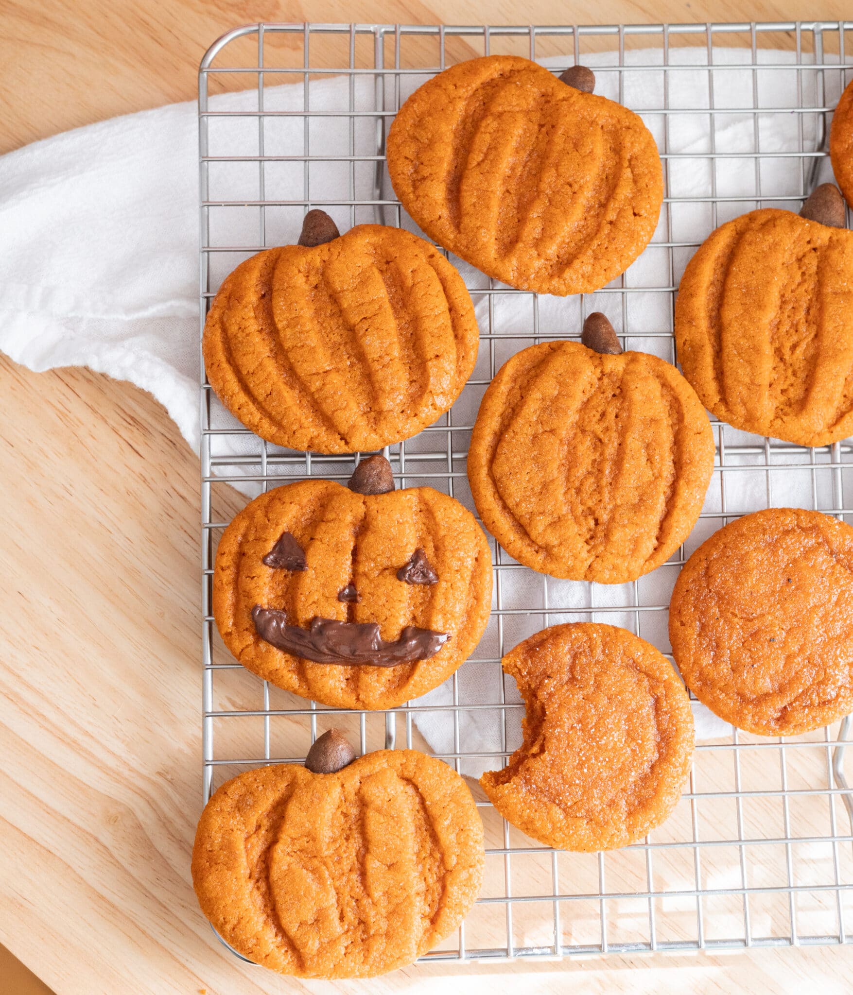 Cute egg-free pumpkin snickerdoodles decorated as jack o'lanterns on a wire rack.