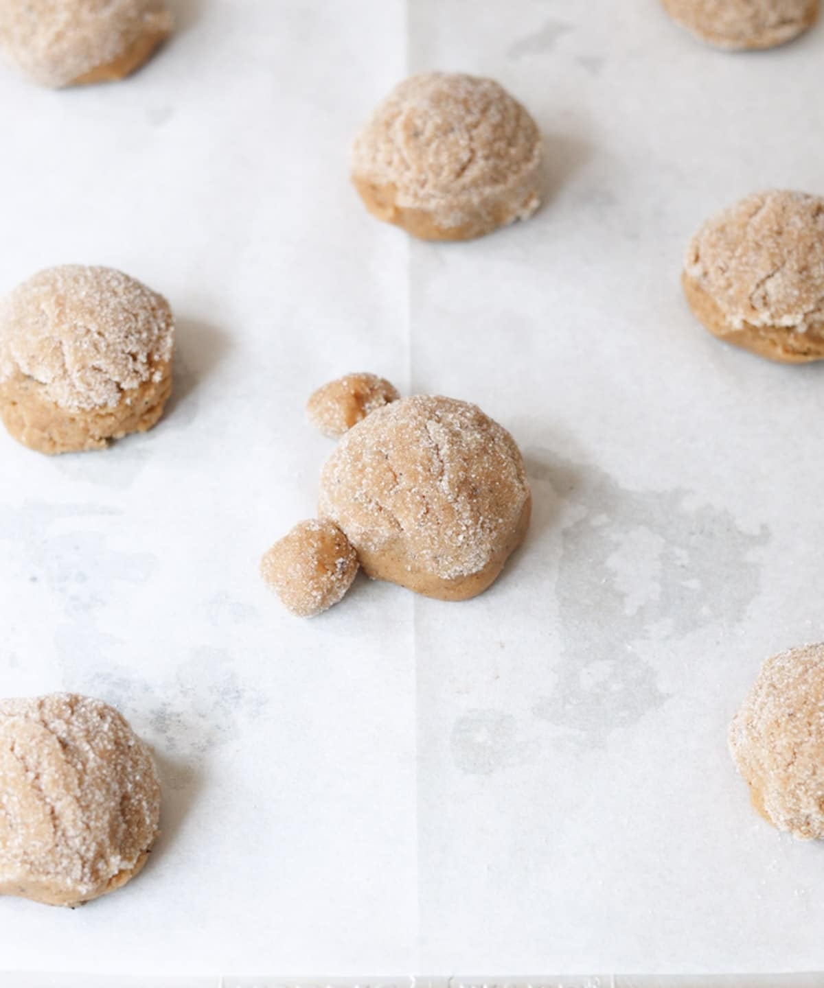 Lined baking sheet with cookie dough balls ready to be baked; one cookie has two smaller dough balls on its sides to bake into a bear cookie.