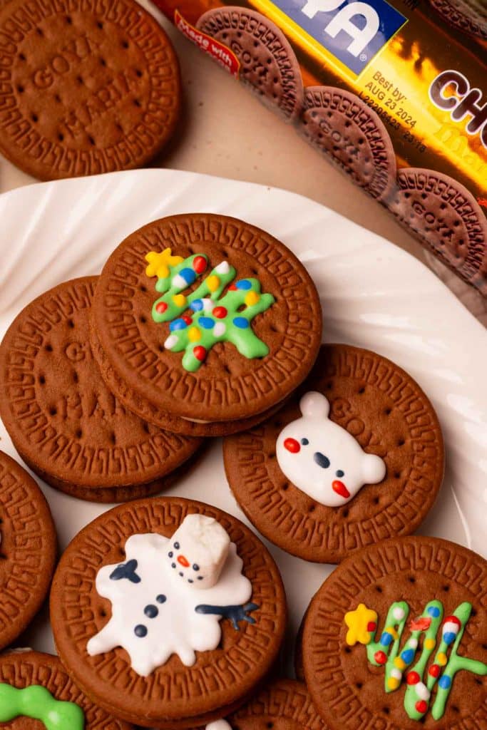 Royal icing chocolate Christmas cookie sandwiches. They are decorated as tree cookies, bear cookies, and snowmen cookies, all on a white plate.