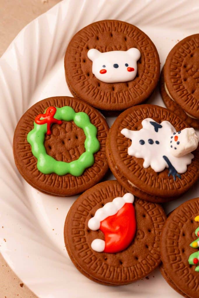 Chocolate Christmas sandwich cookies with maple cream cheese frosting. They're decorated with a wreath, Santa hat, bear, and snowman.