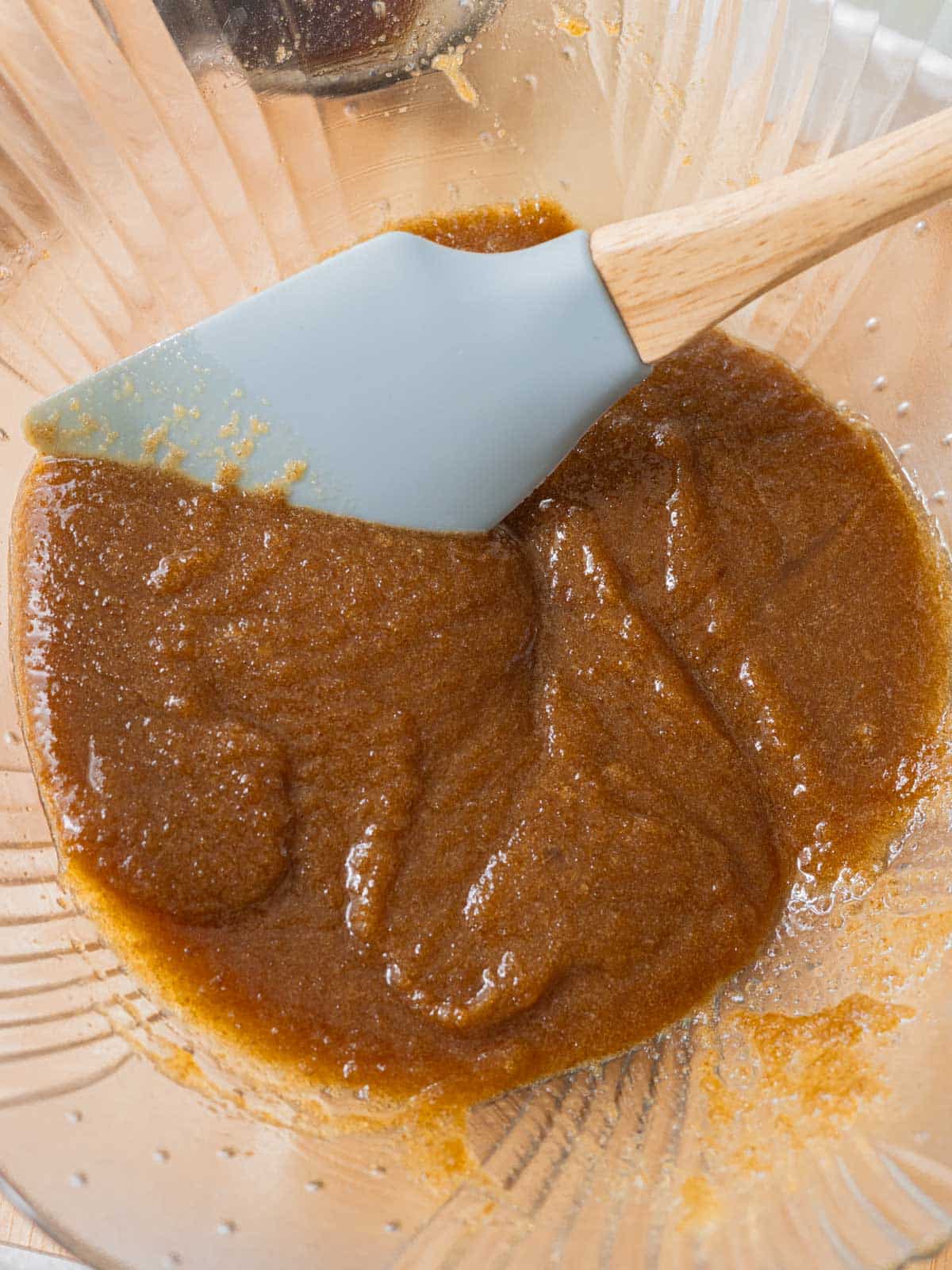 Glass mixing bowl with melted butter and sugars stirred together.