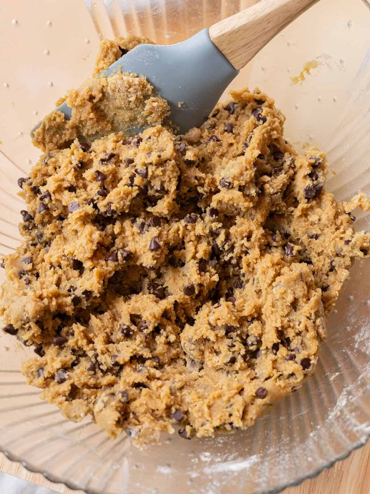 Glass mixing bowl with mini chocolate chip cookie dough batter ready to be scooped.