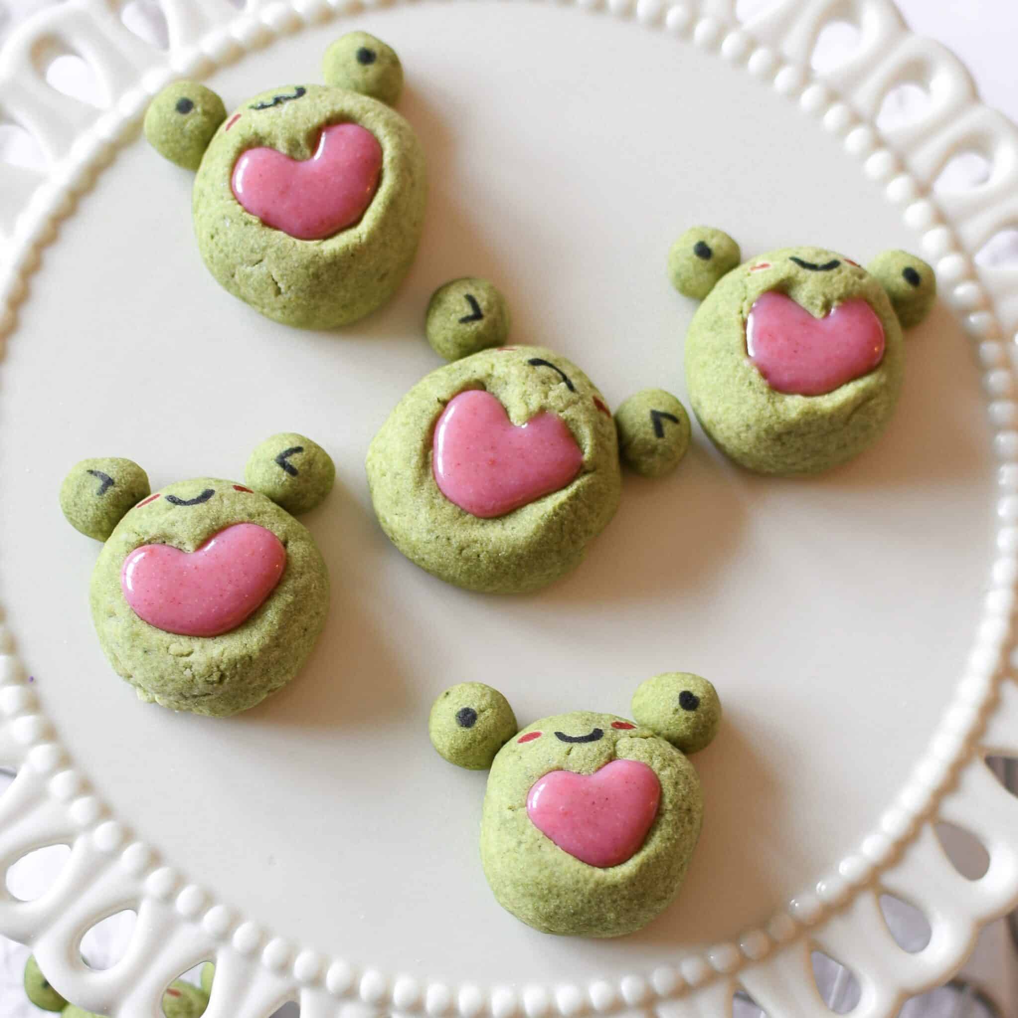 Frog matcha heart thumbprint cookies with strawberry ganache on a cake stand