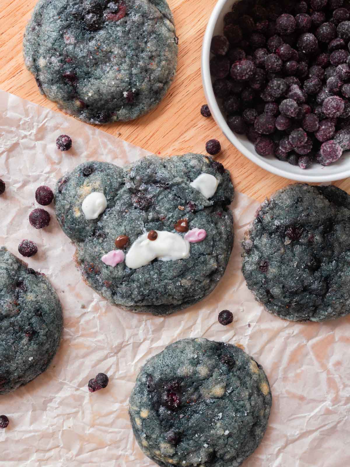 Cute bear-shaped blueberry cookie surrounded by other blueberry cookies on a wooden table.