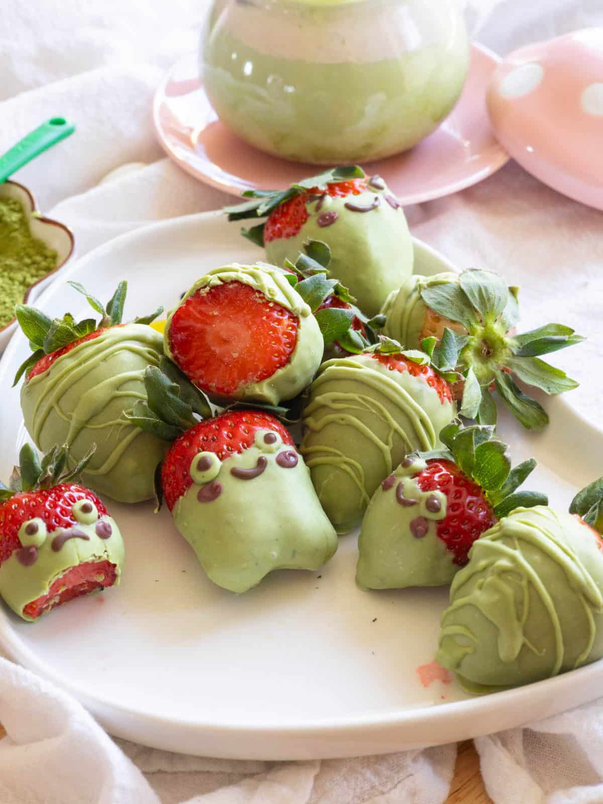 Frog matcha covered strawberries next to an iced matcha latte with strawberry cold foam.