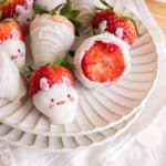 White chocolate-covered strawberries decorated as bunnies on a white plate.