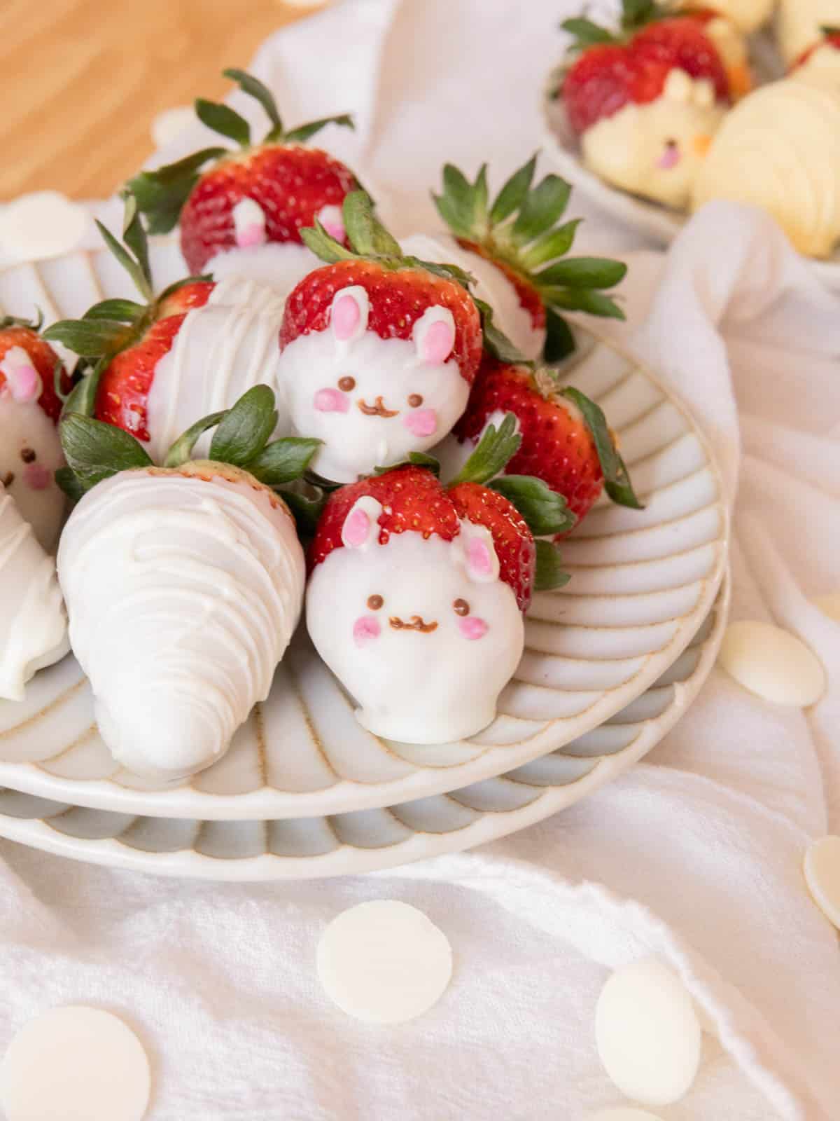 White chocolate-dipped strawberries decorated as bunnies on a white plate.