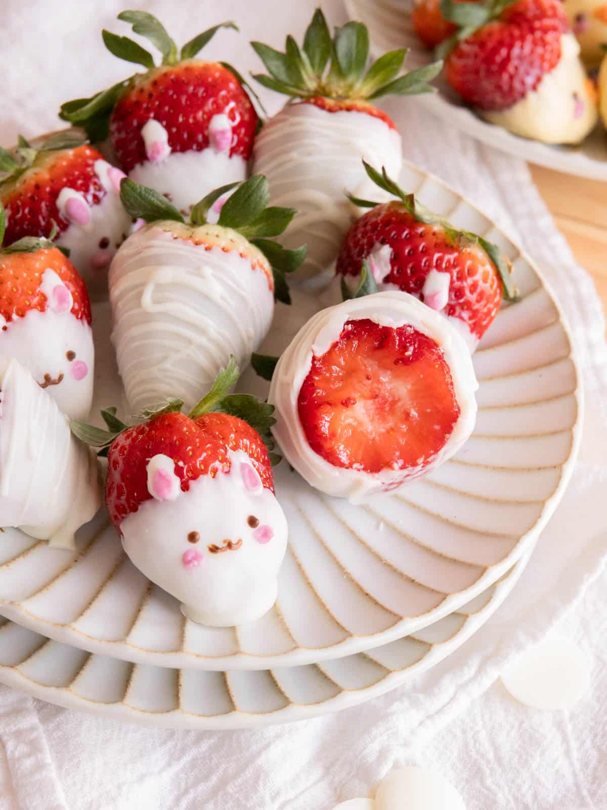 Fresh white chocolate-covered strawberries decorated as cute bunnies on a fluted plate.