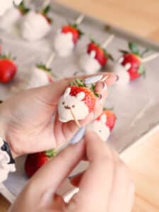 Drawing bunny faces on white chocolate-covered strawberries using melted chocolate and a toothpick.