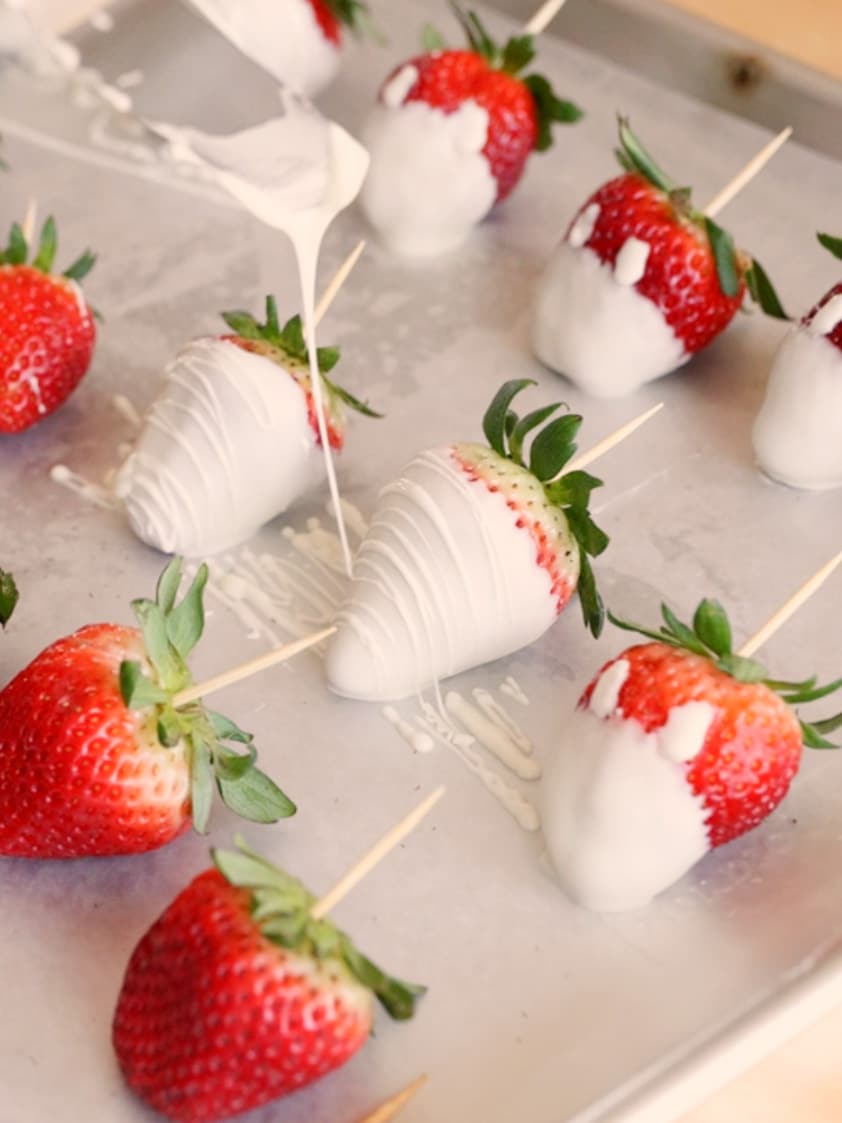 Drizzling white chocolate stripes on white chocolate-covered strawberries.