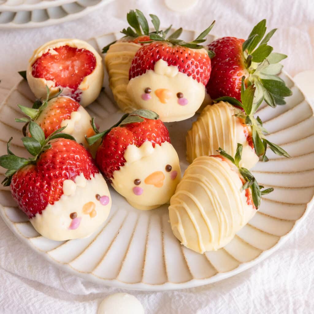 White chocolate-covered strawberries decorated as chicks on a white fluted plate.