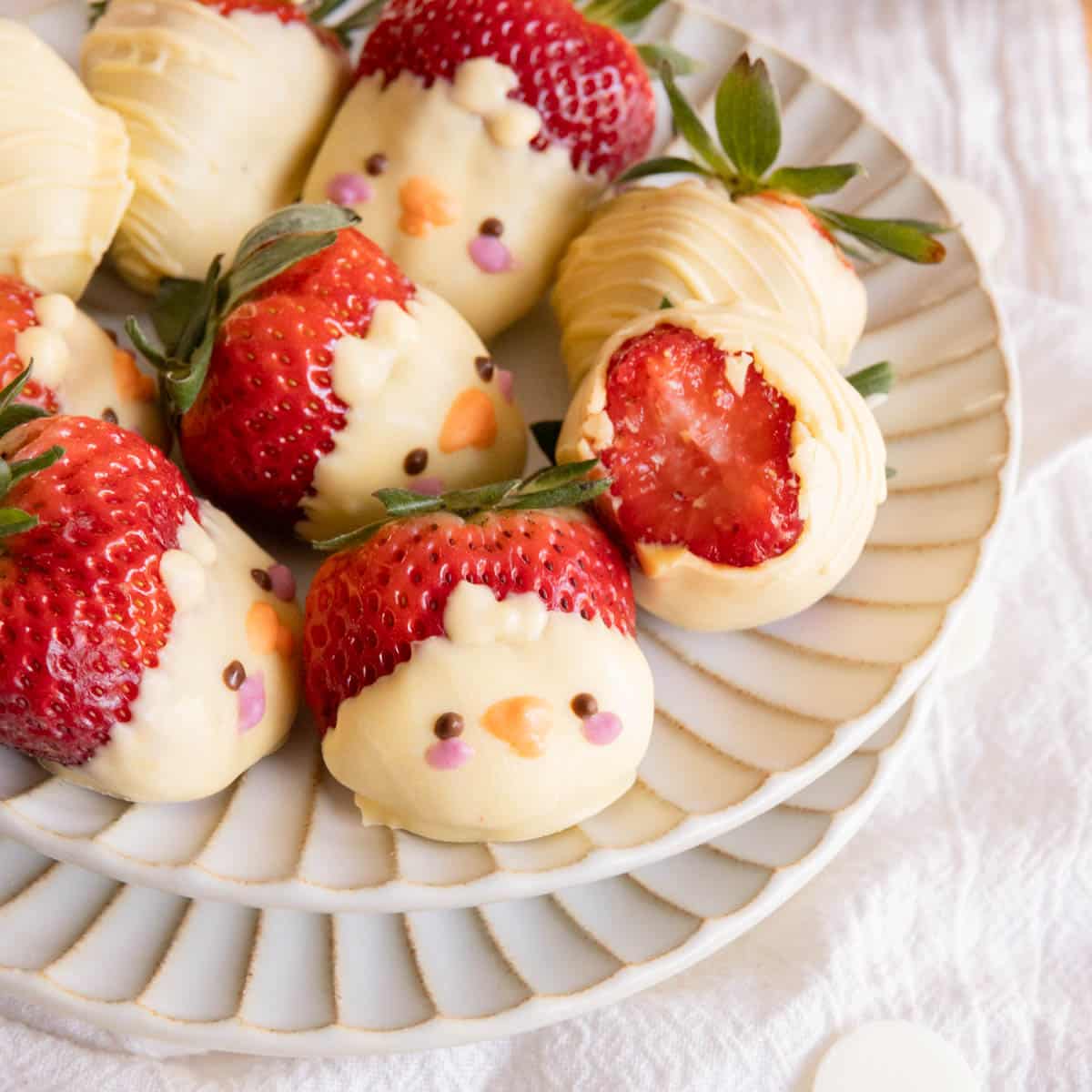 White chocolate-covered strawberries decorated as chicks on a white fluted plate.