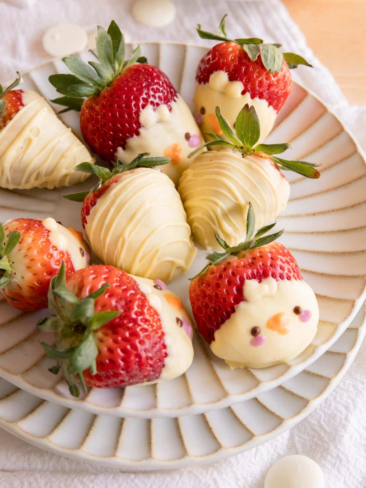 Cute white chocolate-covered strawberries on a white plate, some decorated as chicks.