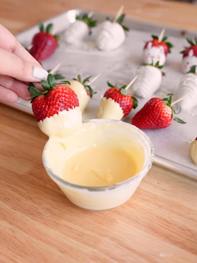 Dipping strawberry halfway into yellow-dyed white chocolate.