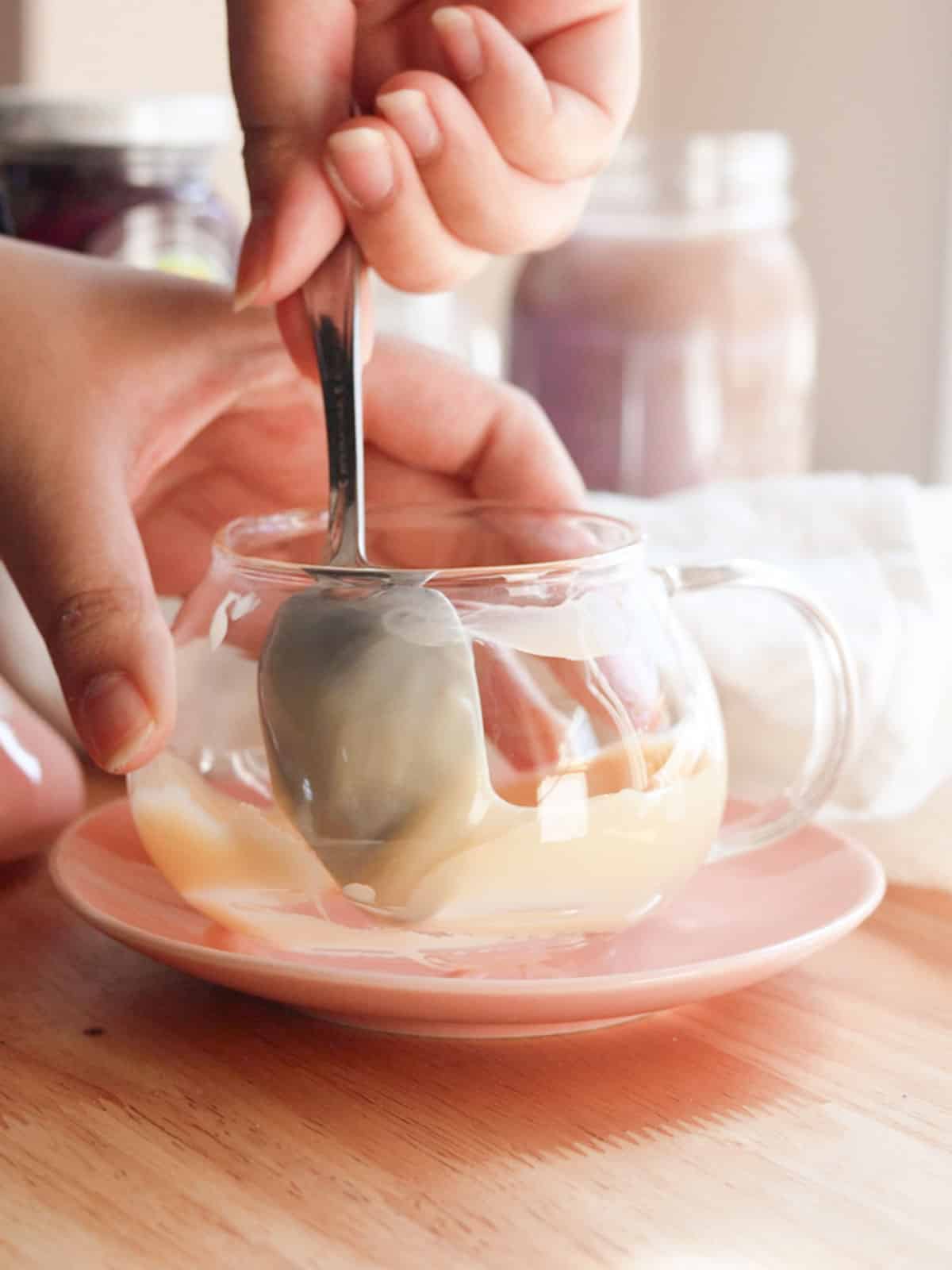 Using a spoon to smear condensed milk on the inside of a glass mug.