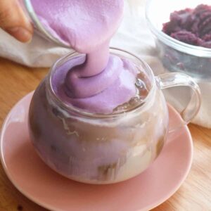 Pouring thick ube cold foam over ube latte.