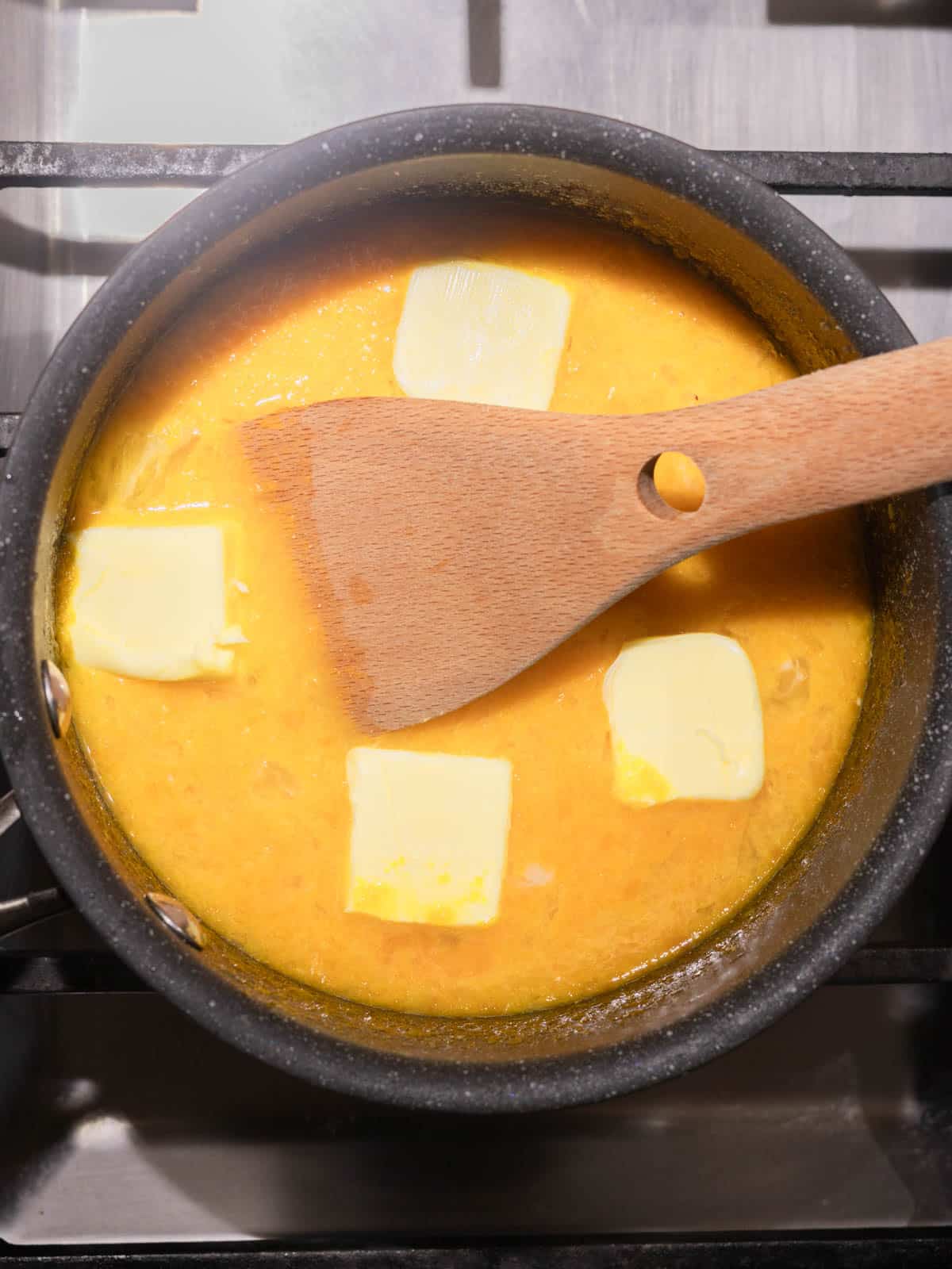 Saucepan with lemon curd ingredients and wooden spatula.