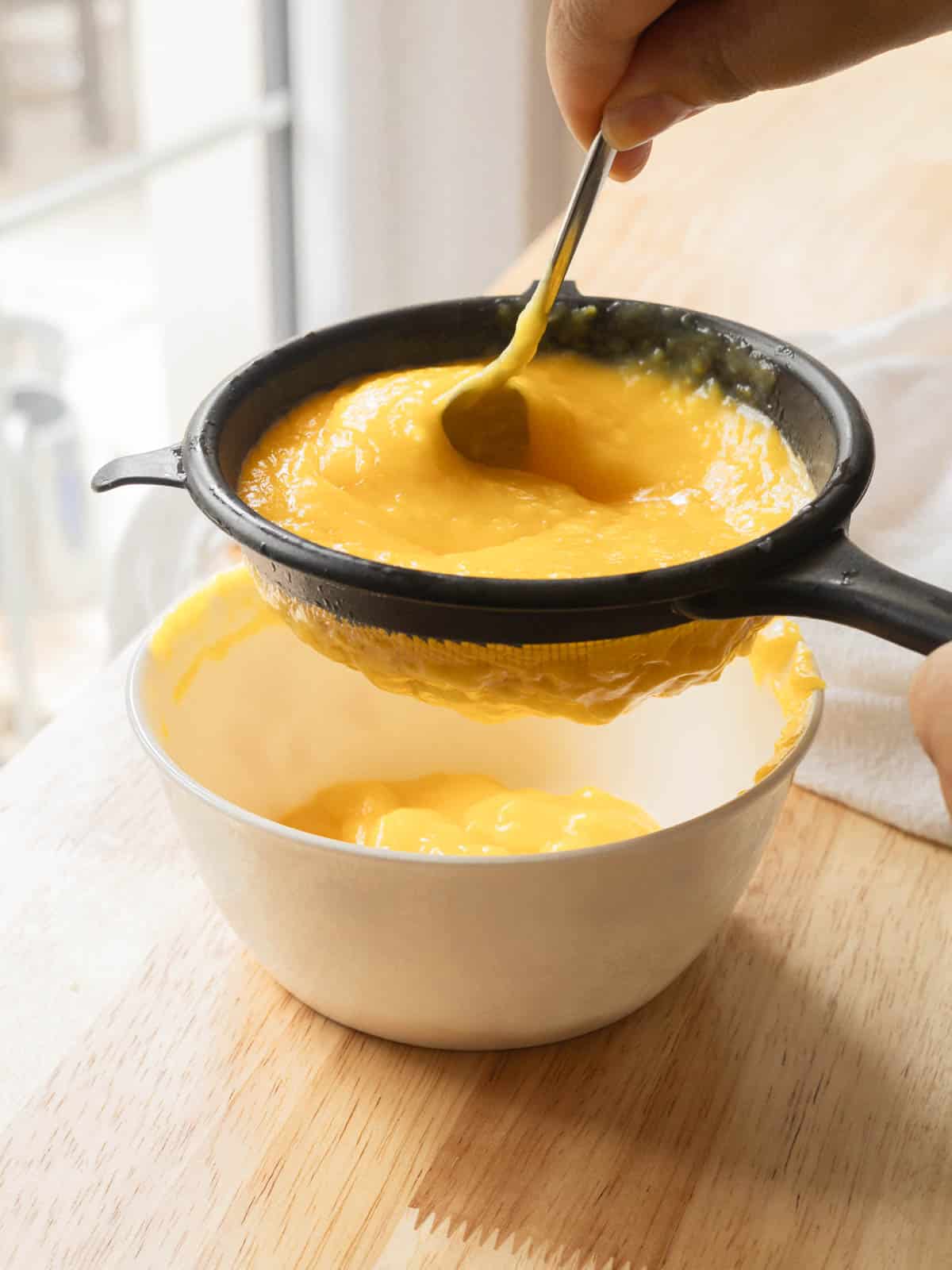 Straining lemon curd through fine mesh sieve. 