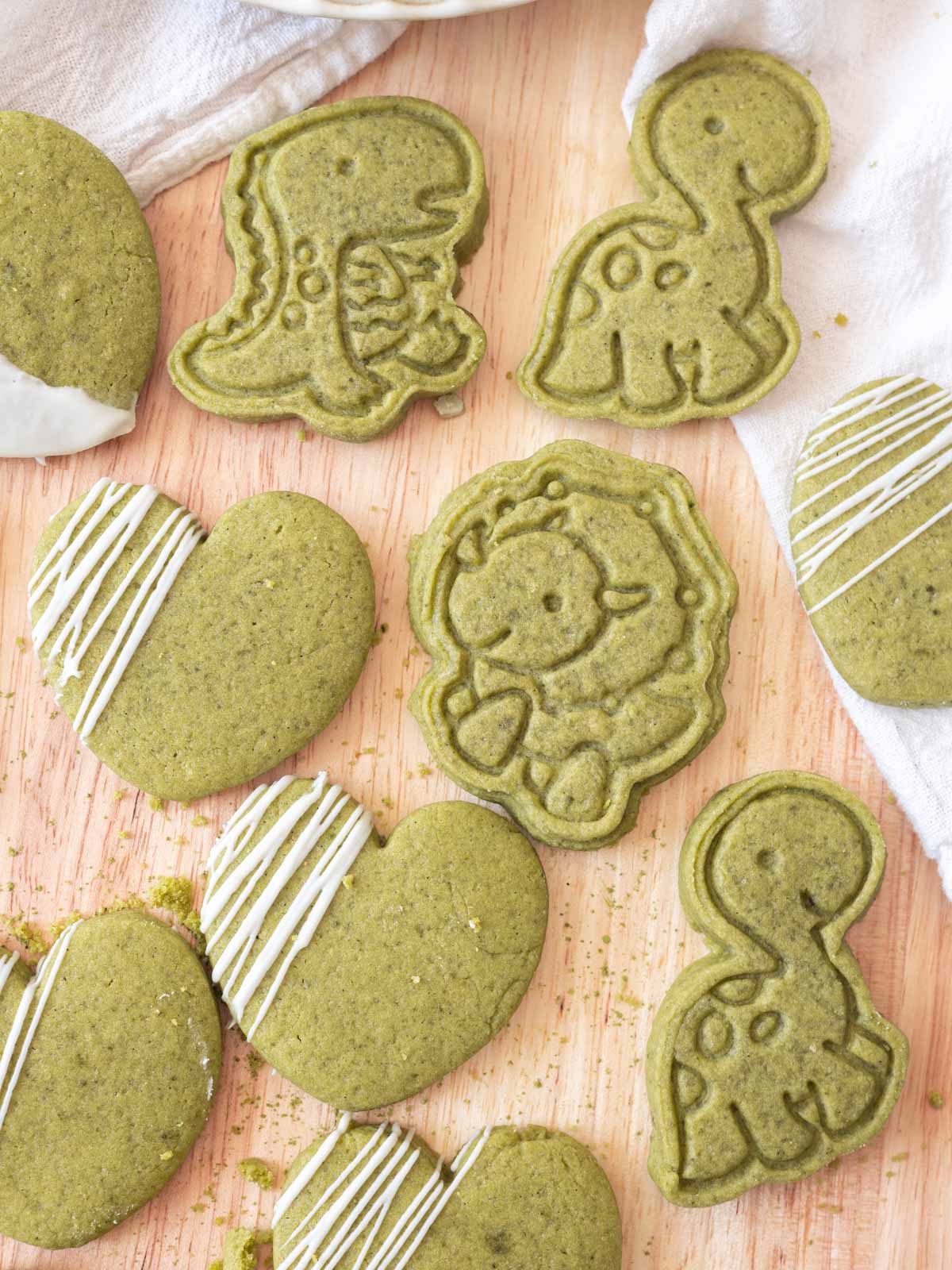 cute heart and dinosaur cookies made out of matcha cookie dough, on a wooden backdrop.