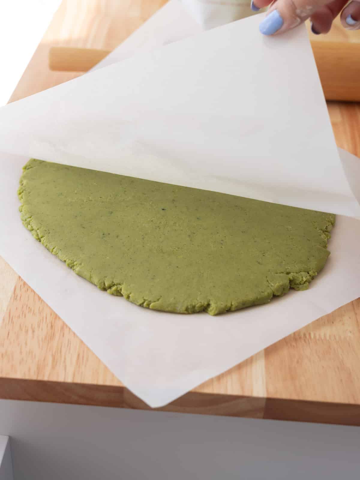 Parchment paper stack with rolled out matcha cookie dough in the middle.