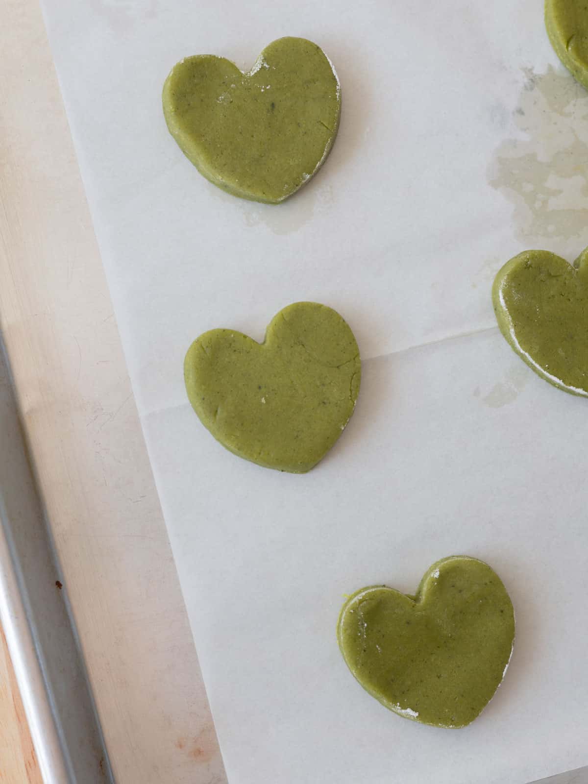 Matcha cookie hearts on lined baking tray, ready to be baked.