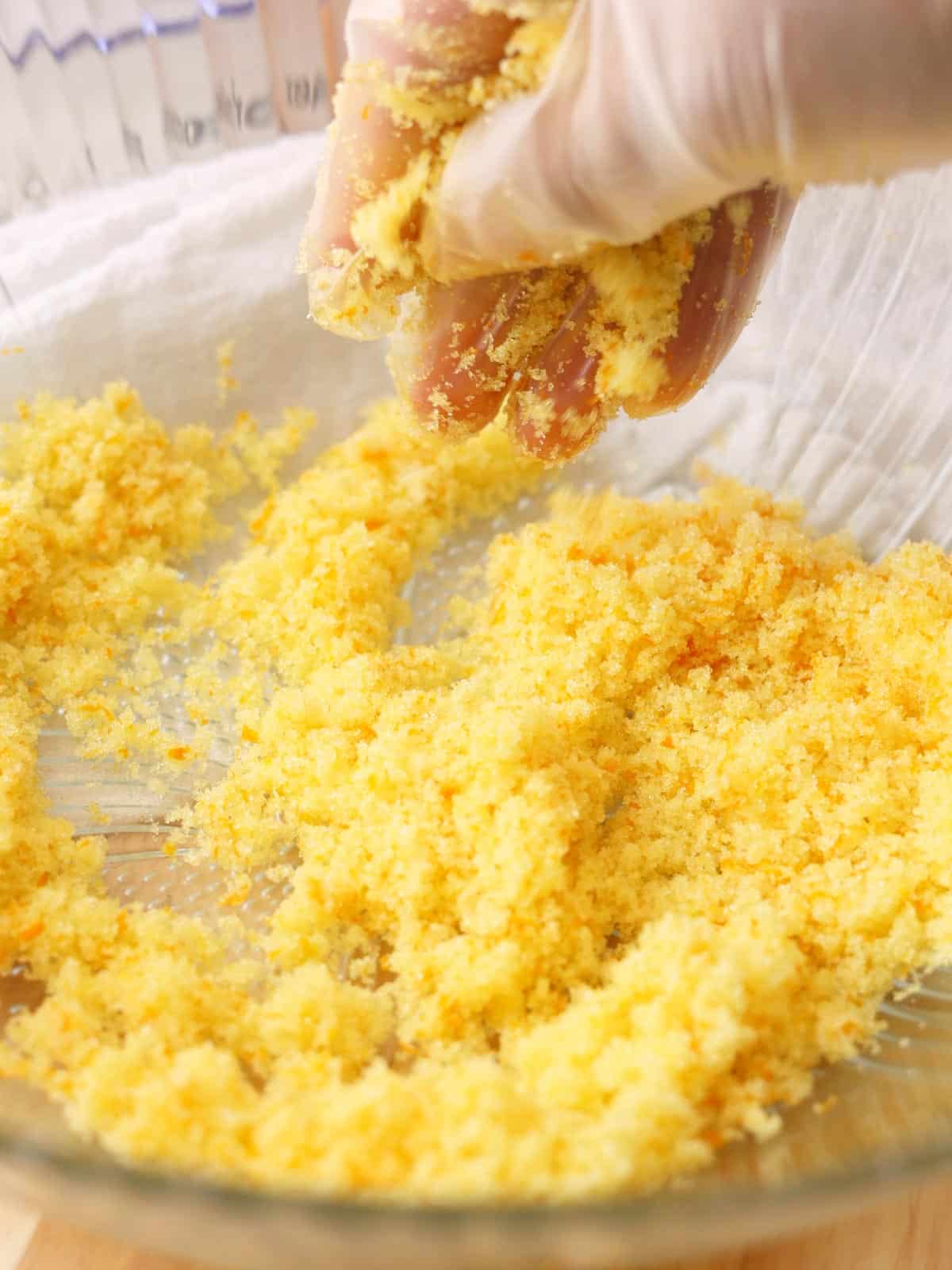 Mixing orange zest and granulated sugar with a gloved hand in a glass mixing bowl.