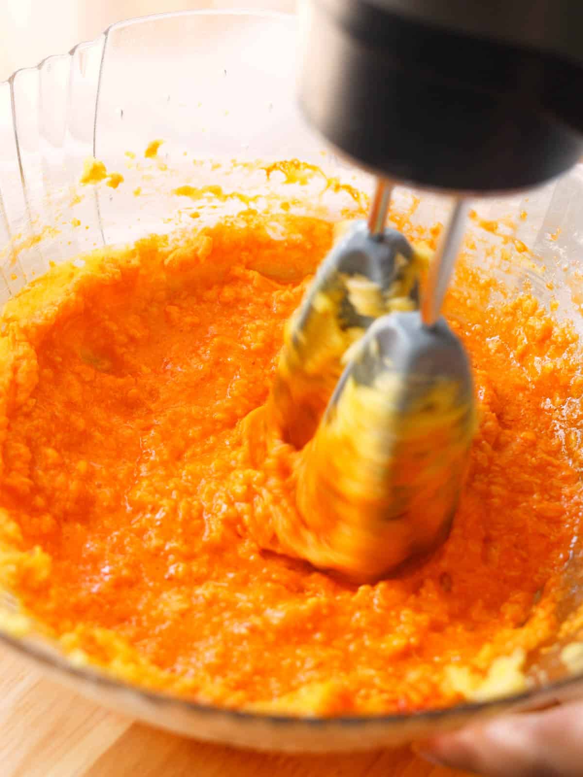 Mixing vibrant orange-colored batter with mixer.